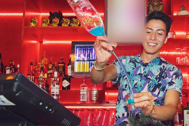 A bartender pouring a cocktail at the red-lit Asian Beer Cafe bar