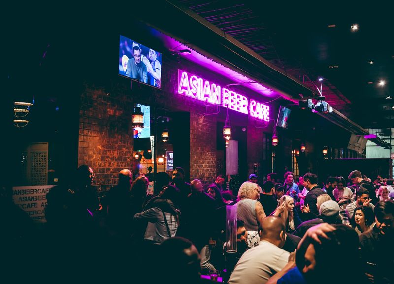 A packed room under the pink Asian Beer Cafe neon sign